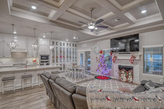 living room with ceiling fan, beam ceiling, a tile fireplace, and coffered ceiling