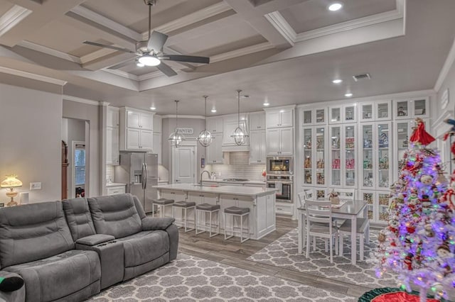 living room with coffered ceiling, sink, light hardwood / wood-style flooring, ceiling fan, and beamed ceiling