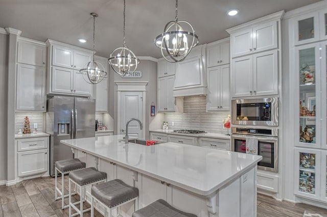 kitchen with sink, an island with sink, a kitchen bar, white cabinets, and appliances with stainless steel finishes