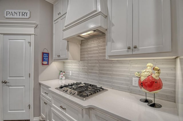 kitchen featuring white cabinets, custom range hood, decorative backsplash, and stainless steel gas stovetop