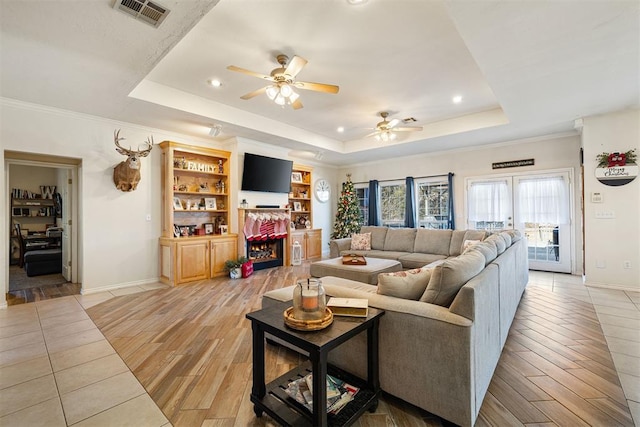 living room with a fireplace, a raised ceiling, ceiling fan, and ornamental molding