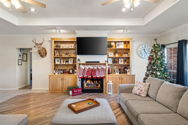 living room featuring a tray ceiling, crown molding, ceiling fan, and light hardwood / wood-style floors