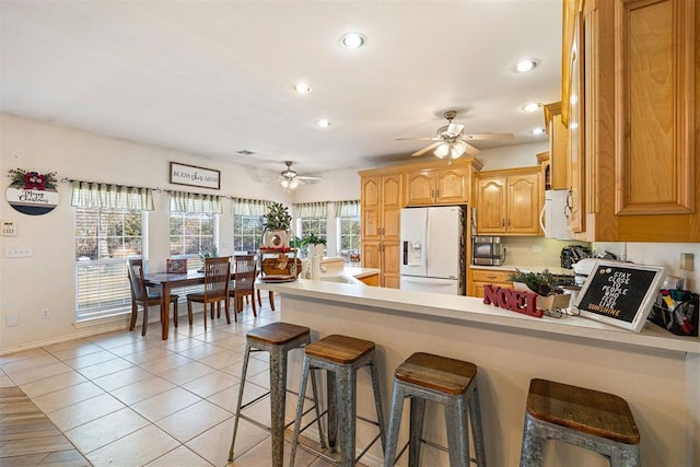 kitchen with white appliances, ceiling fan, light tile patterned floors, kitchen peninsula, and a breakfast bar area