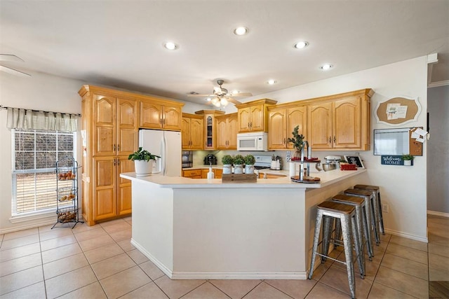 kitchen with a kitchen breakfast bar, ceiling fan, white appliances, and kitchen peninsula