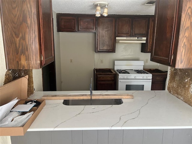 kitchen featuring light stone countertops, kitchen peninsula, a textured ceiling, dark brown cabinetry, and white gas stove