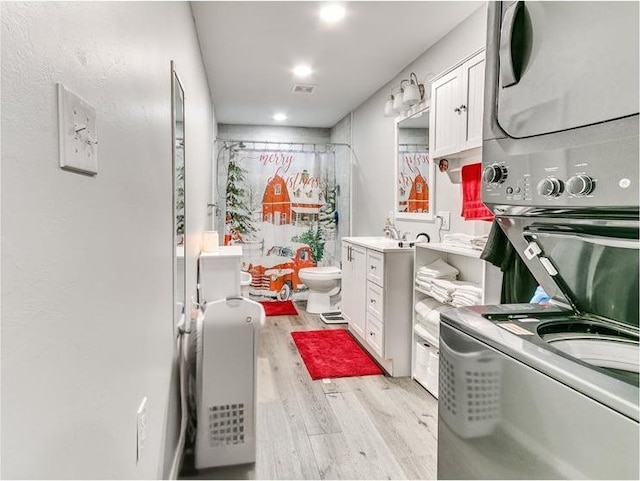 kitchen with white cabinets, light hardwood / wood-style floors, and stacked washer and clothes dryer