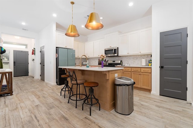 kitchen featuring white cabinetry, stainless steel appliances, hanging light fixtures, and an island with sink