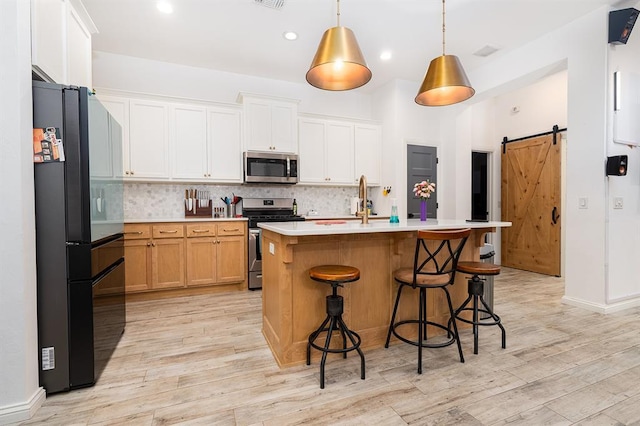 kitchen with hanging light fixtures, a barn door, an island with sink, tasteful backsplash, and stainless steel appliances