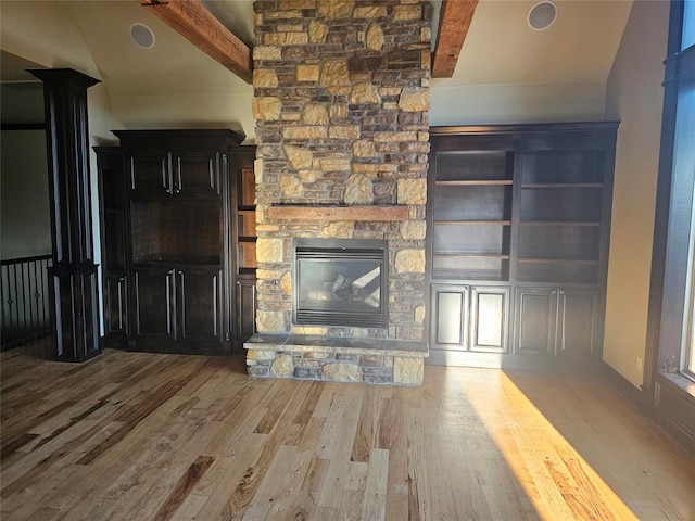 unfurnished living room with beam ceiling, a stone fireplace, and light hardwood / wood-style floors