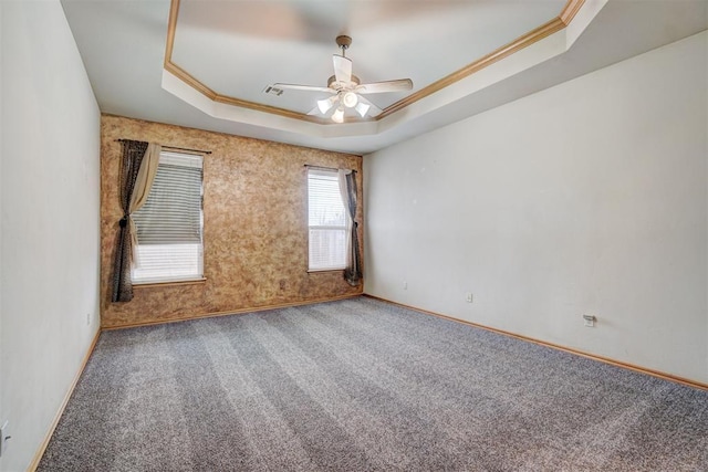 empty room featuring a raised ceiling, ceiling fan, carpet flooring, and crown molding