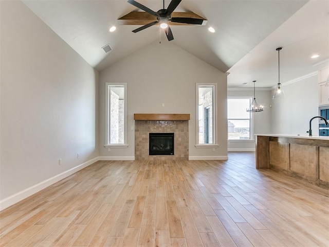 unfurnished living room featuring ceiling fan with notable chandelier, sink, light wood-type flooring, a fireplace, and ornamental molding
