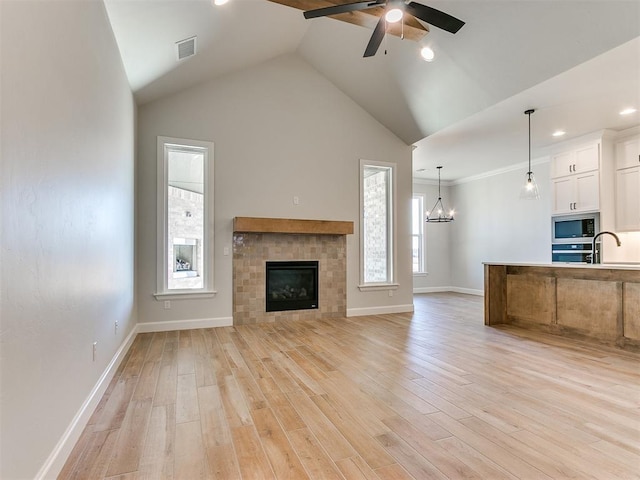 unfurnished living room with ceiling fan with notable chandelier, light hardwood / wood-style floors, crown molding, and a tiled fireplace