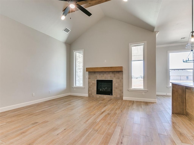 unfurnished living room featuring a tiled fireplace, ceiling fan, plenty of natural light, and light wood-type flooring