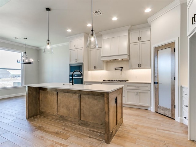 kitchen featuring a center island with sink, decorative light fixtures, white cabinetry, stainless steel gas cooktop, and a chandelier