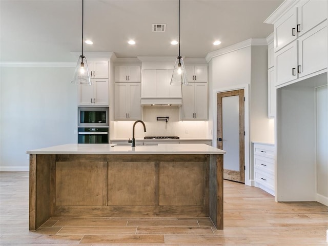 kitchen with built in microwave, stainless steel oven, hanging light fixtures, a center island with sink, and white cabinets