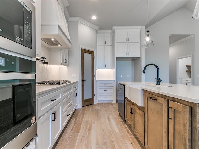 kitchen featuring pendant lighting, custom exhaust hood, white cabinets, light hardwood / wood-style flooring, and stainless steel appliances