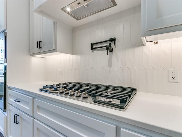 kitchen featuring tasteful backsplash, white cabinetry, black oven, stainless steel gas stovetop, and range hood
