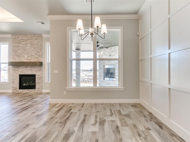 unfurnished dining area featuring a tile fireplace, ceiling fan with notable chandelier, light hardwood / wood-style flooring, and ornamental molding