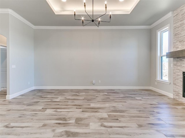 unfurnished dining area featuring a raised ceiling, a stone fireplace, light hardwood / wood-style floors, and a notable chandelier