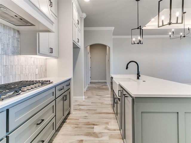 kitchen with hanging light fixtures, crown molding, an island with sink, decorative backsplash, and custom exhaust hood