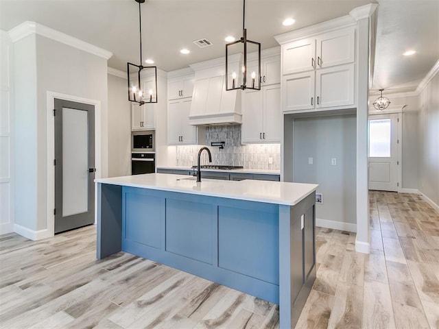 kitchen featuring appliances with stainless steel finishes, custom range hood, decorative light fixtures, a center island with sink, and white cabinetry