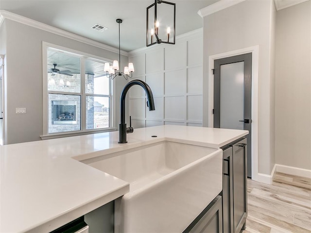 kitchen with sink, hanging light fixtures, crown molding, ceiling fan with notable chandelier, and light wood-type flooring