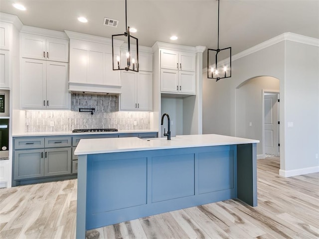 kitchen featuring stainless steel gas cooktop, crown molding, pendant lighting, white cabinetry, and an island with sink