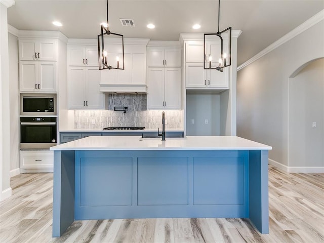 kitchen featuring a center island with sink, white cabinets, stainless steel appliances, and decorative light fixtures