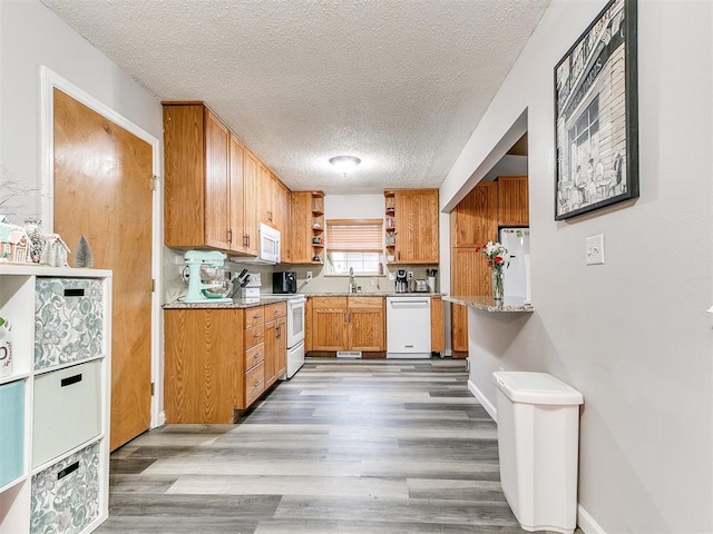 kitchen featuring tasteful backsplash, light stone counters, a textured ceiling, white appliances, and light hardwood / wood-style flooring