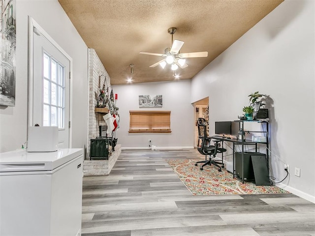 office with ceiling fan, a fireplace, a textured ceiling, and light hardwood / wood-style flooring