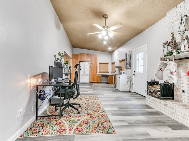 home office featuring a textured ceiling, ceiling fan, light hardwood / wood-style flooring, and vaulted ceiling