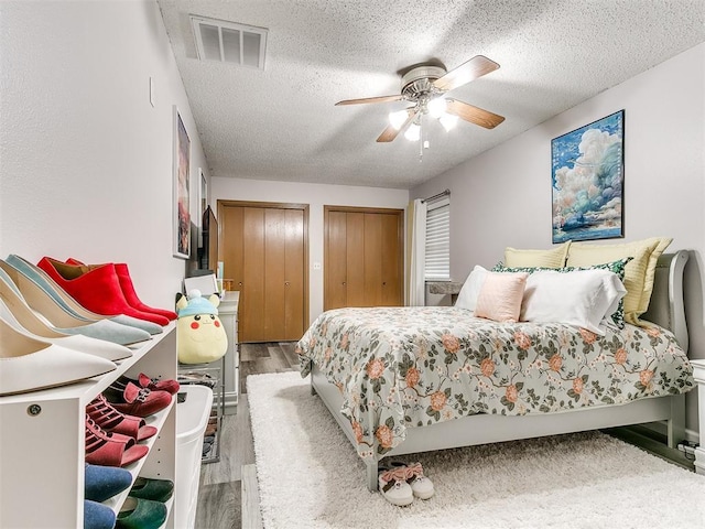 bedroom featuring wood-type flooring, a textured ceiling, two closets, and ceiling fan