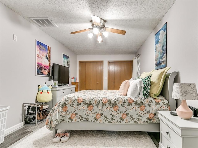 bedroom with hardwood / wood-style floors, ceiling fan, a textured ceiling, and two closets