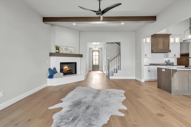 living room featuring ceiling fan, beam ceiling, light hardwood / wood-style floors, and a fireplace