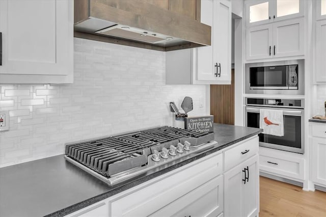 kitchen with appliances with stainless steel finishes, tasteful backsplash, wall chimney exhaust hood, light hardwood / wood-style flooring, and white cabinetry