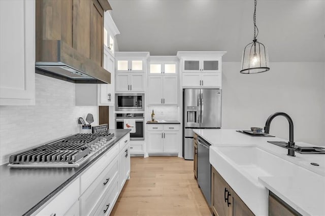 kitchen with white cabinets, hanging light fixtures, wall chimney range hood, and appliances with stainless steel finishes