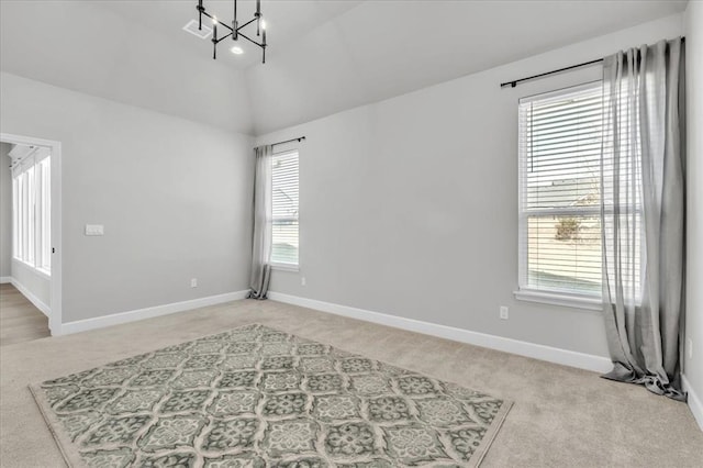 empty room with light colored carpet, high vaulted ceiling, plenty of natural light, and a notable chandelier