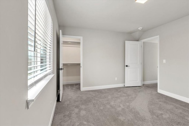 unfurnished bedroom featuring a walk in closet, a closet, and light colored carpet