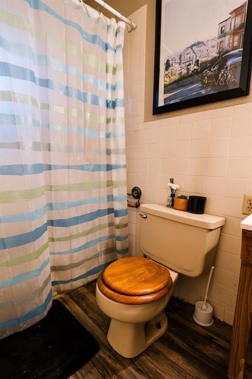 bathroom with toilet, hardwood / wood-style flooring, vanity, tile walls, and a shower with shower curtain