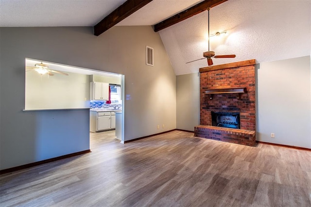 unfurnished living room featuring a fireplace, lofted ceiling with beams, light hardwood / wood-style floors, and a textured ceiling