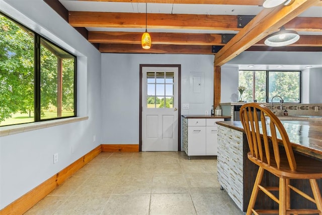 interior space with beamed ceiling, white cabinetry, hanging light fixtures, and a healthy amount of sunlight