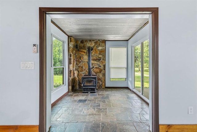 unfurnished sunroom featuring a healthy amount of sunlight, a wood stove, and wooden ceiling