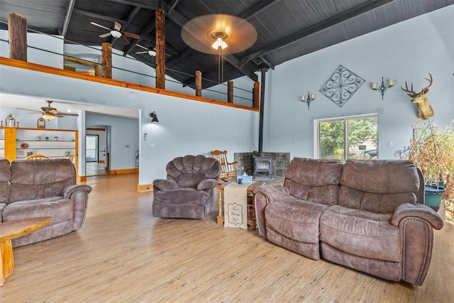 living room featuring a wood stove, ceiling fan, beamed ceiling, high vaulted ceiling, and light wood-type flooring