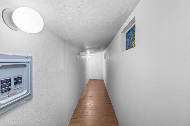 hallway with hardwood / wood-style floors, a textured ceiling, and electric panel