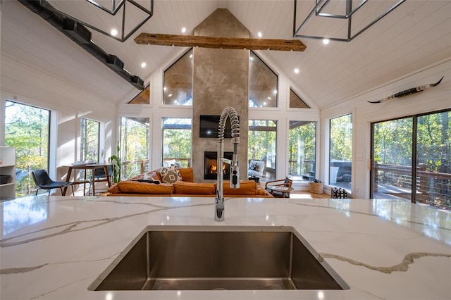 kitchen featuring high vaulted ceiling, sink, light stone countertops, a large fireplace, and beam ceiling