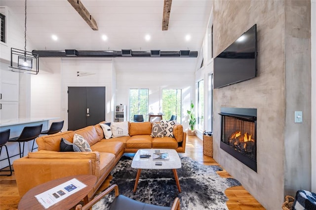 living room with beamed ceiling, a large fireplace, and light hardwood / wood-style flooring