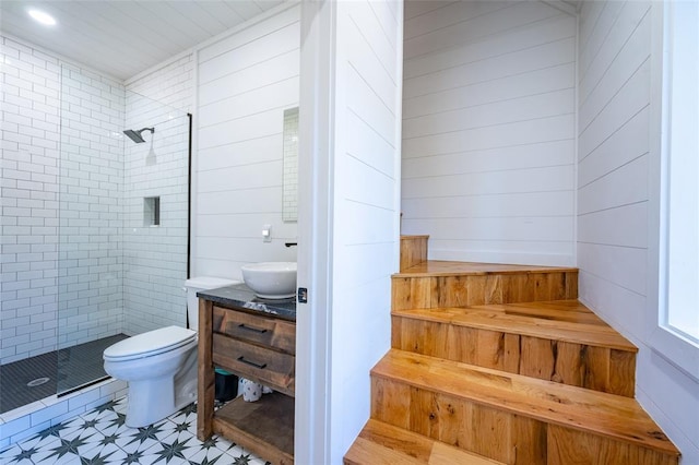 bathroom featuring a tile shower, vanity, toilet, and wood walls