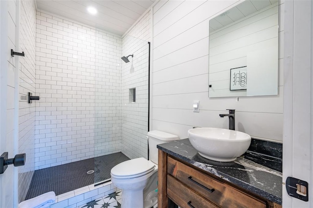 bathroom featuring wooden walls, vanity, toilet, and a tile shower