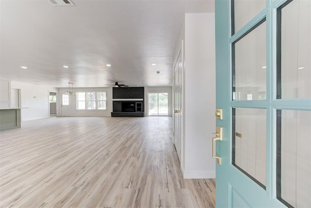 unfurnished living room with ceiling fan, a fireplace, and light wood-type flooring