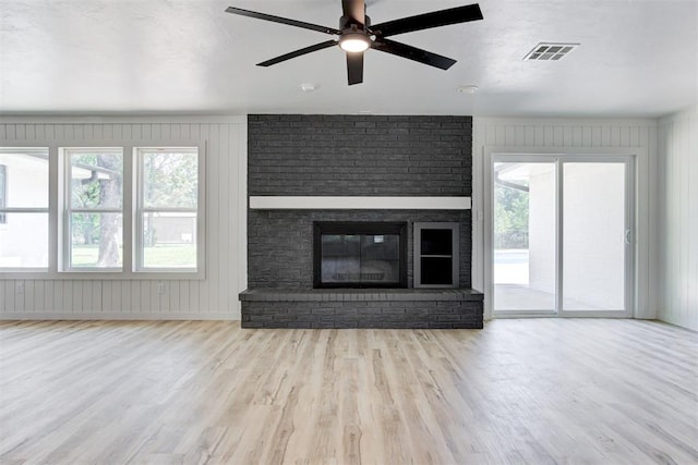 unfurnished living room with light wood-type flooring, a brick fireplace, ceiling fan, and wooden walls